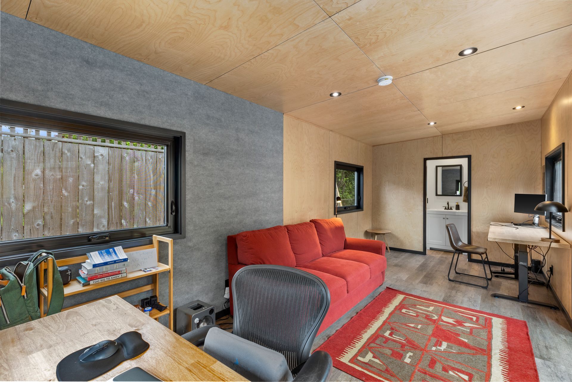 A living room with a red couch, desk, and chairs.