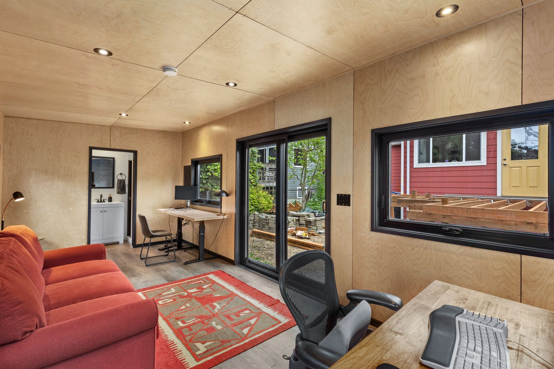 A living room with a couch, desk, chair, and sliding glass doors.