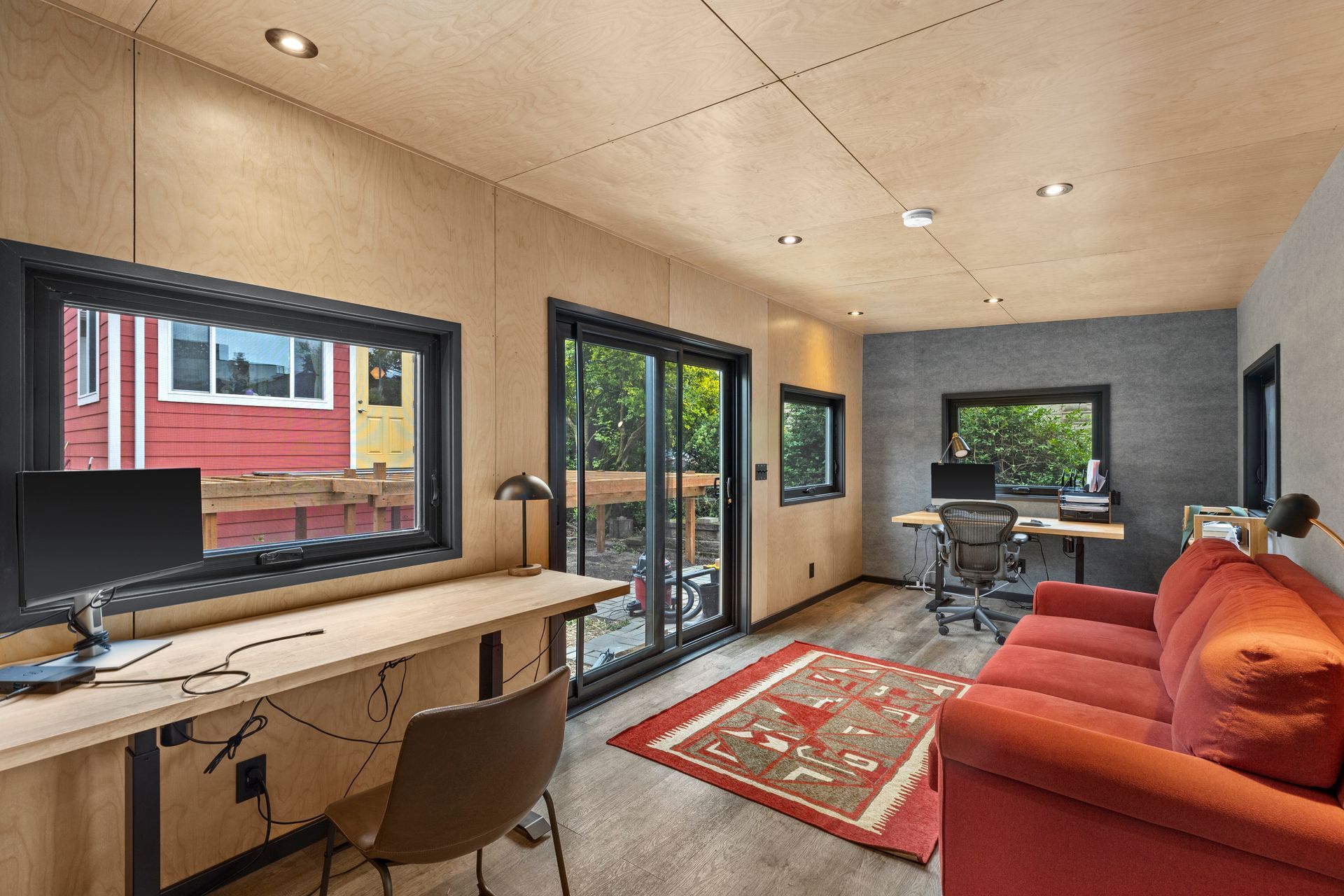 A living room with a red couch, desk, chair, and computer.