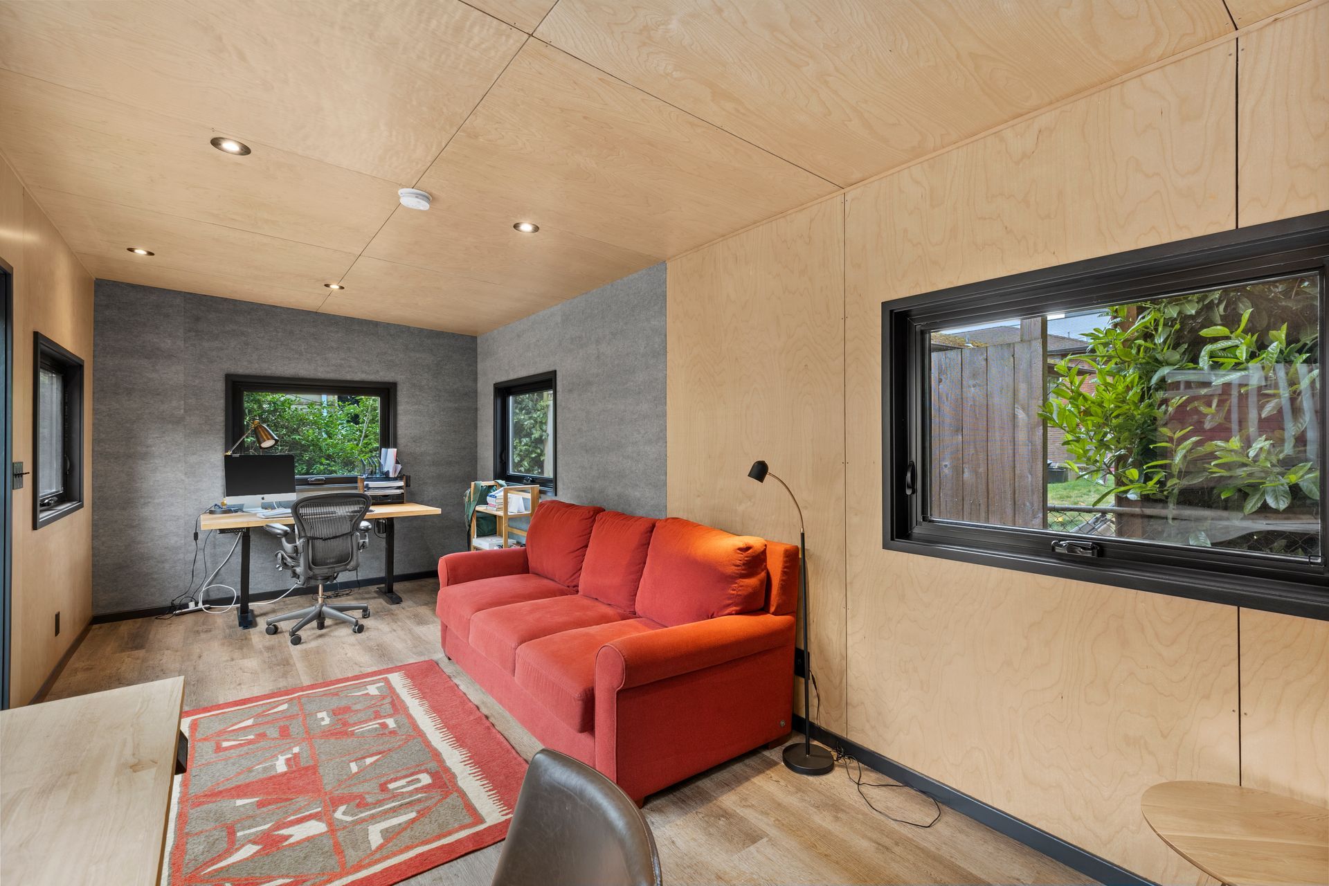 A living room with a red couch and a desk.