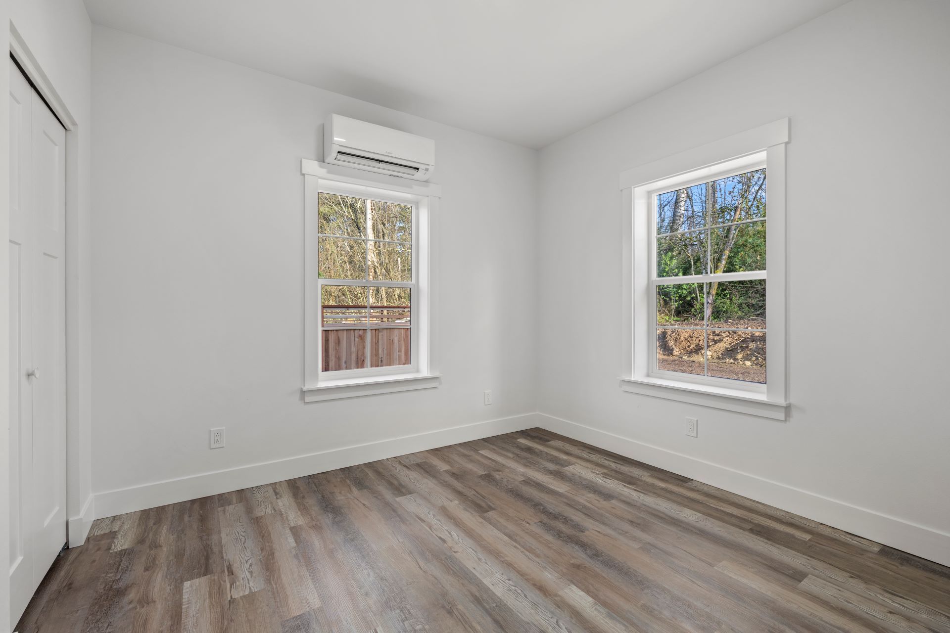 An empty bedroom with hardwood floors and two windows.