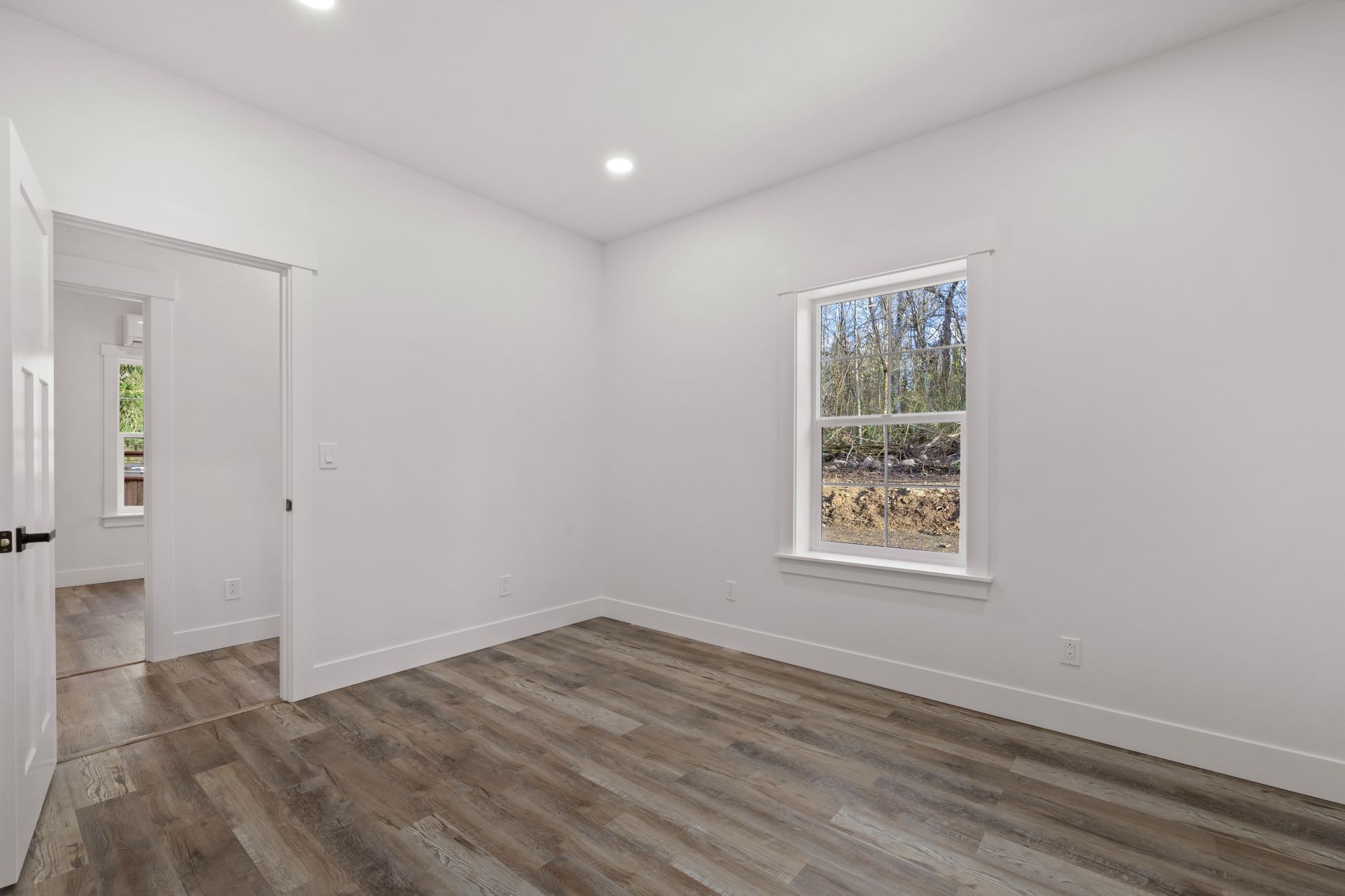 An empty bedroom with hardwood floors and a window.