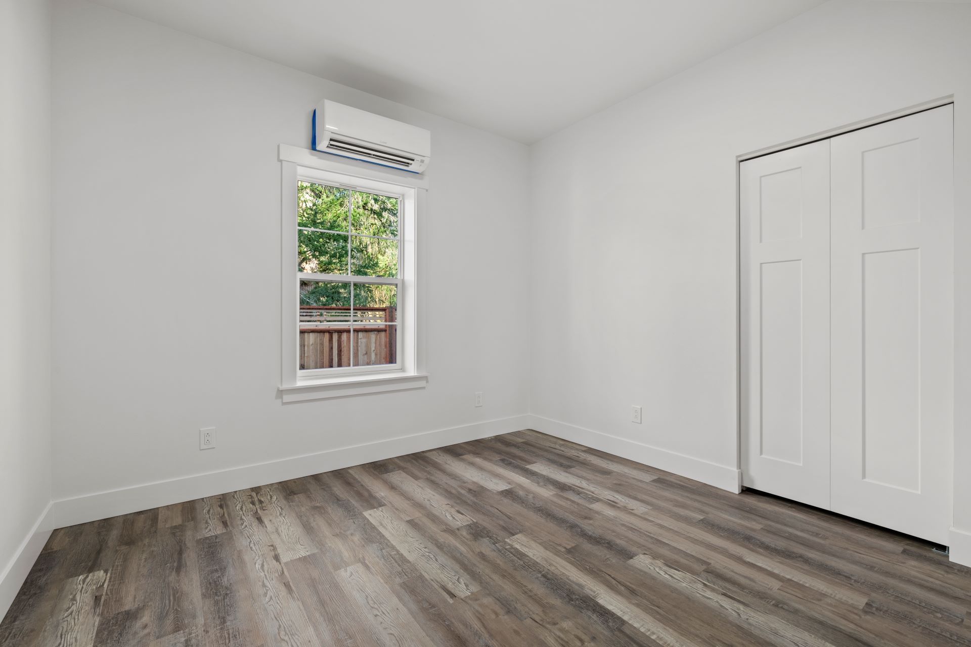 An empty bedroom with hardwood floors and a window.