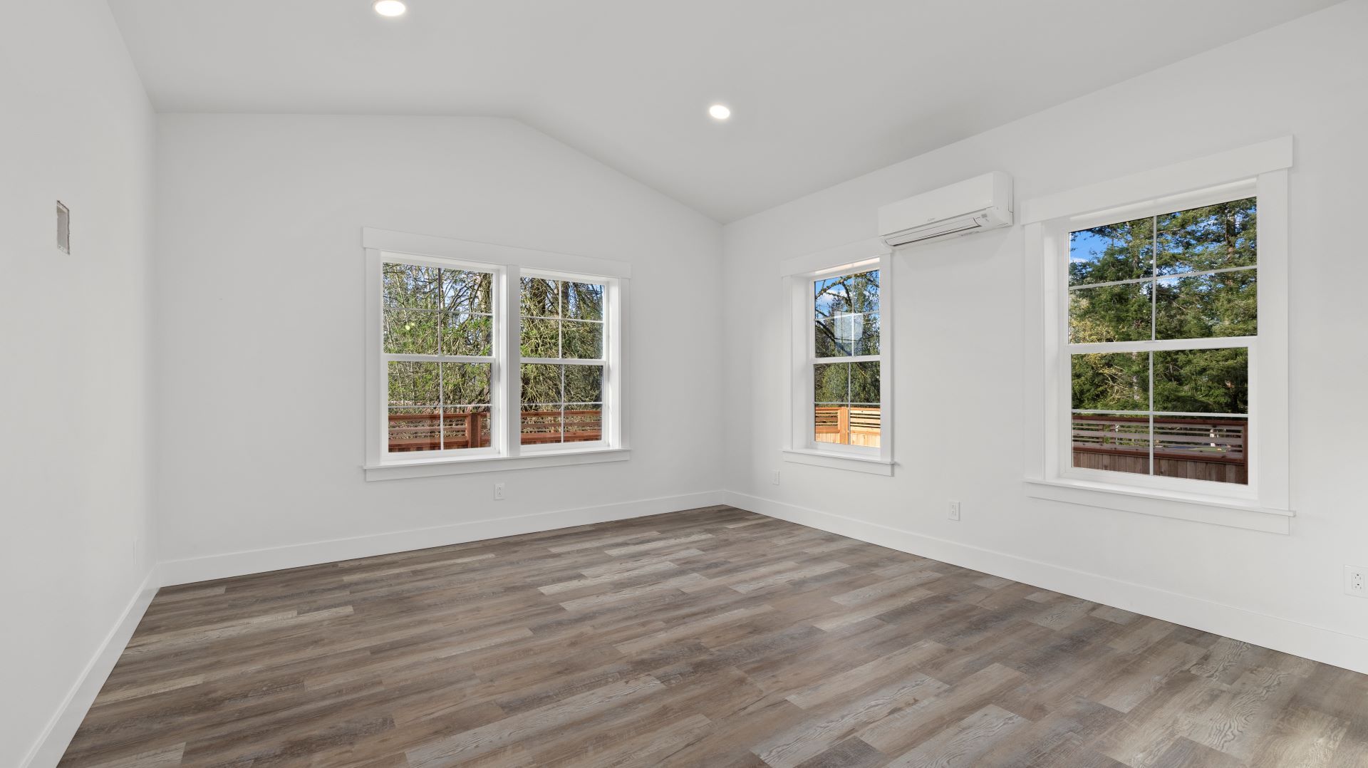 An empty living room with hardwood floors and two windows.