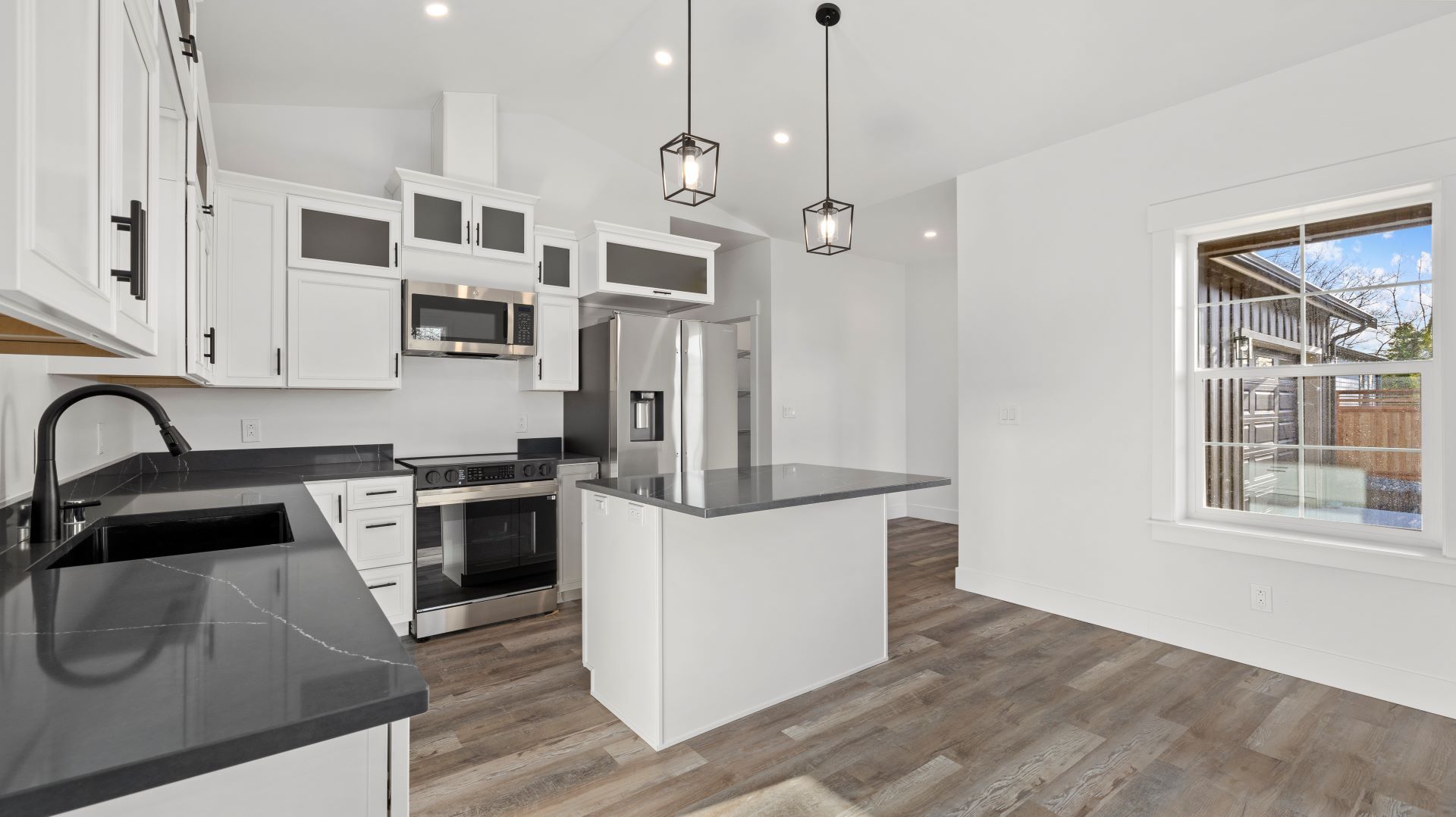 A kitchen with white cabinets , stainless steel appliances , granite counter tops and a large island.
