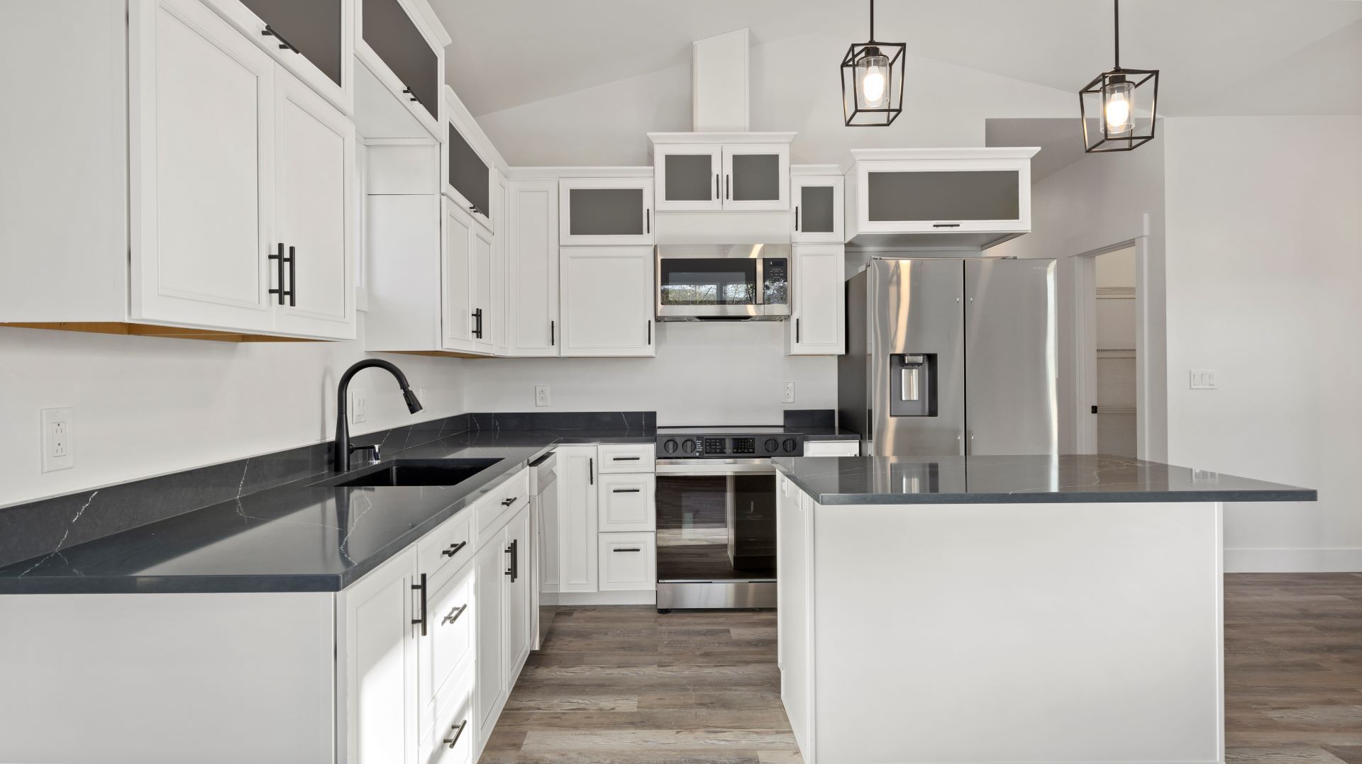 A kitchen with white cabinets , black counter tops , stainless steel appliances and a large island.
