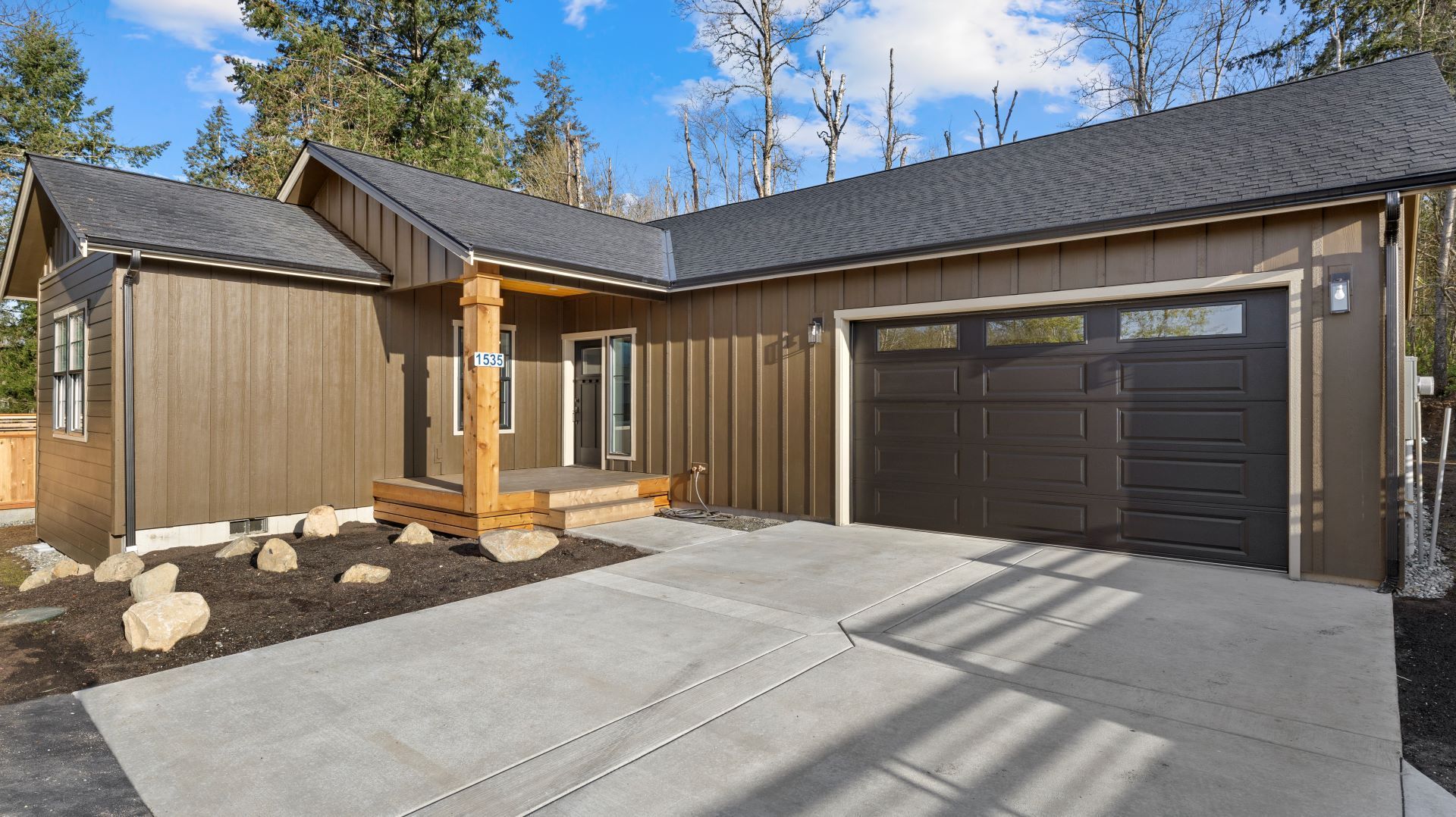 A brown house with a black garage door and a concrete driveway