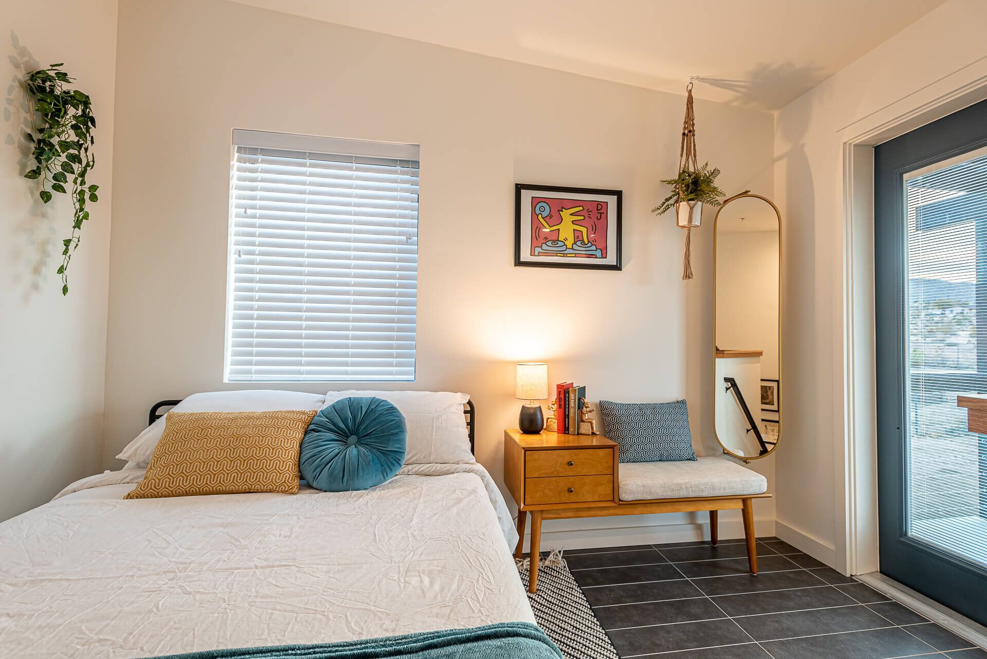 A bedroom with a bed, nightstand, bench, and mirror.