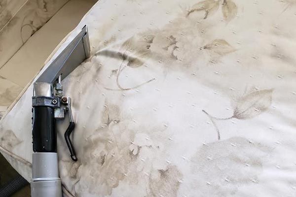 a vacuum cleaner is cleaning a dirty pillow on a couch.