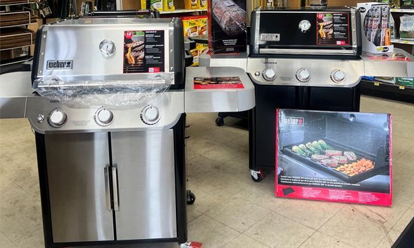 Two gas grills were displayed in a store, one stainless steel, one black.