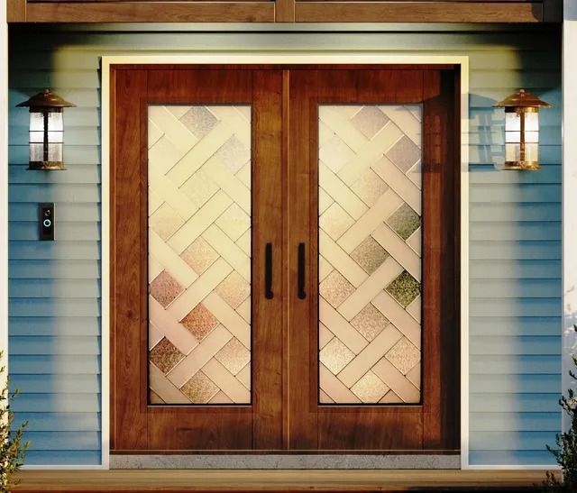 Double wooden front doors with frosted, basket-weave patterned glass panels, framed by blue siding and wall-mounted lamps.