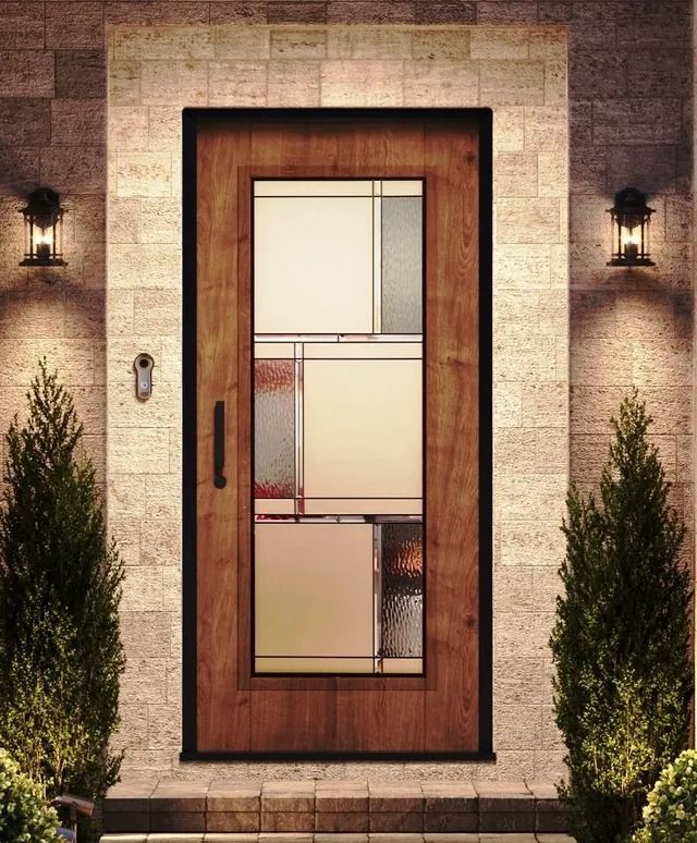 A wood-toned front door with a vertical, multi-paned glass window, flanked by two small trees and wall-mounted lanterns.