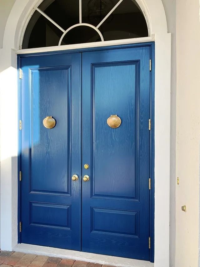 A pair of dark blue double doors with gold scallop-shaped knockers and a semi-circular transom window above.