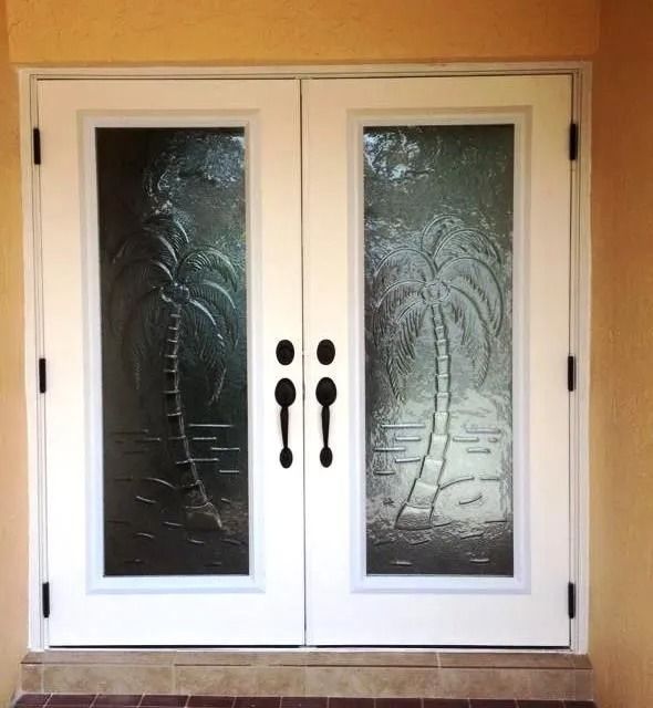A set of white double front doors featuring decorative glass panels etched with palm tree designs and black door handles.