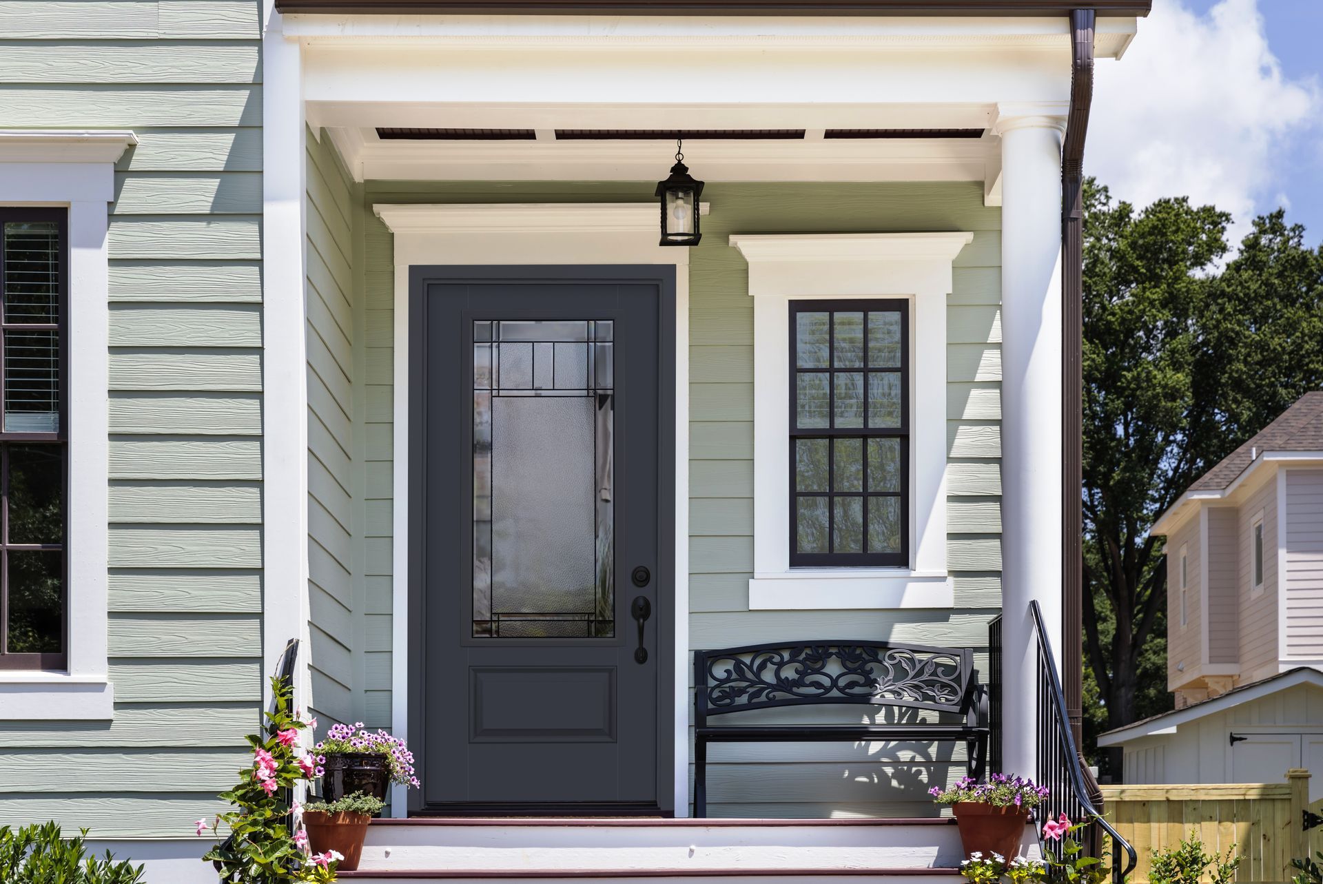 A covered porch with light green siding features a dark grey front door, a small window, and a black metal bench.