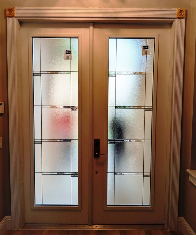 Wooden double front door with frosted glass panels and black handle, framed by trim indoors