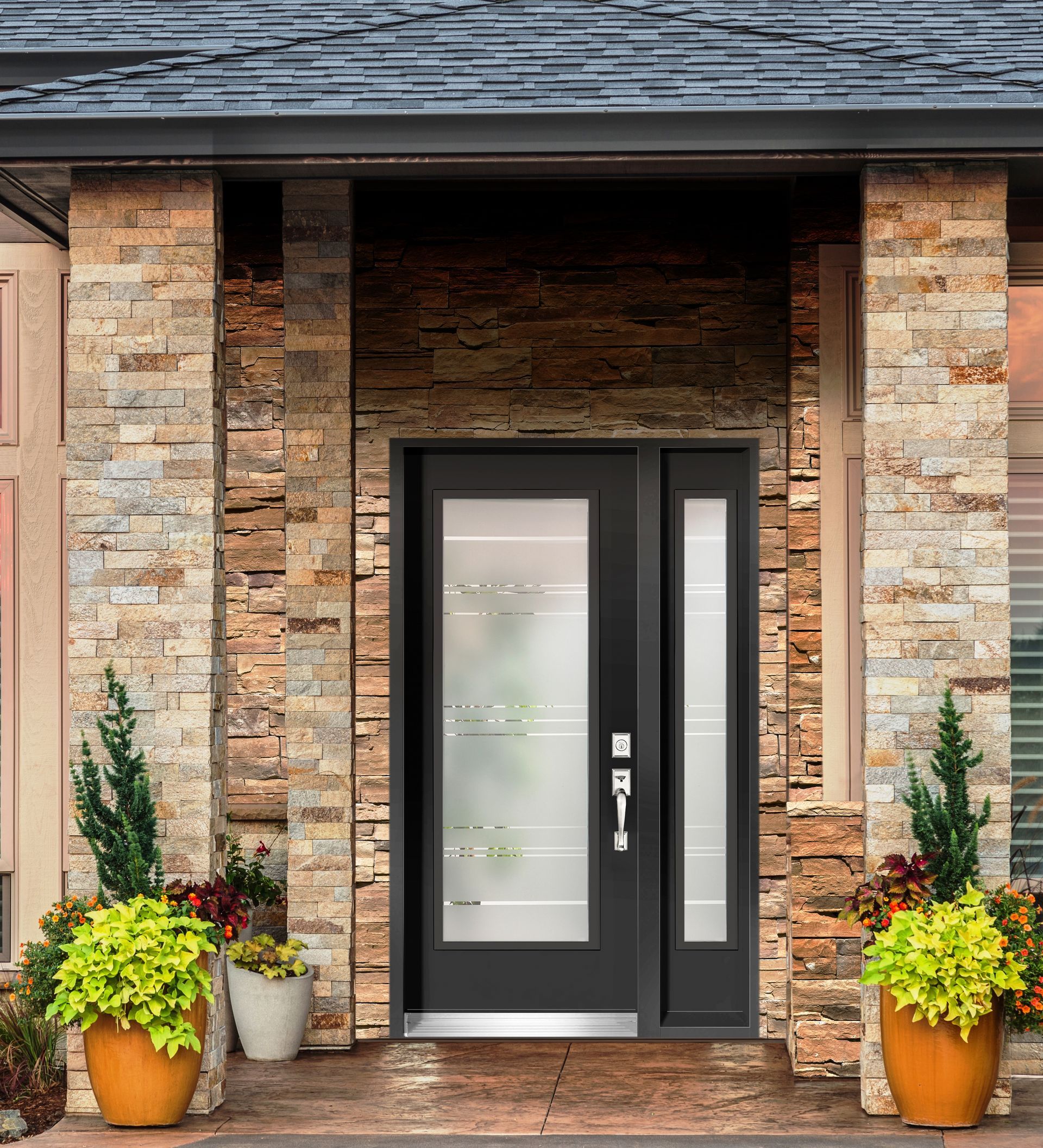 A modern dark door with glass panels and side light, centered between two stone pillars with potted plants on a porch.