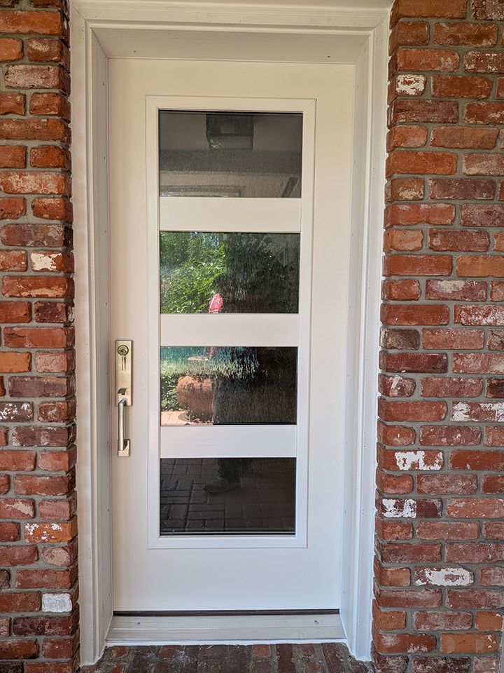 White front door with four frosted glass panels set in a brick exterior wall.