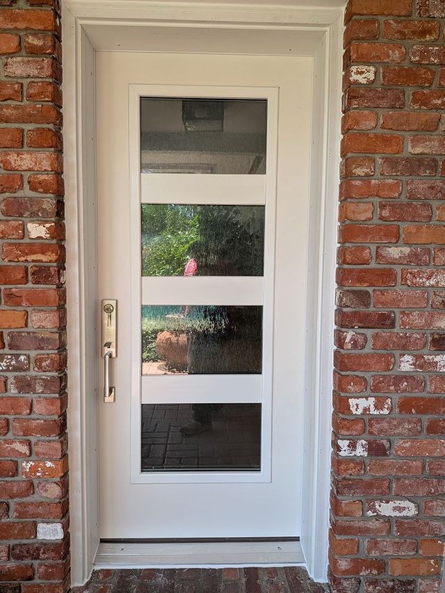 White front door with four frosted glass panels set in a brick exterior wall.