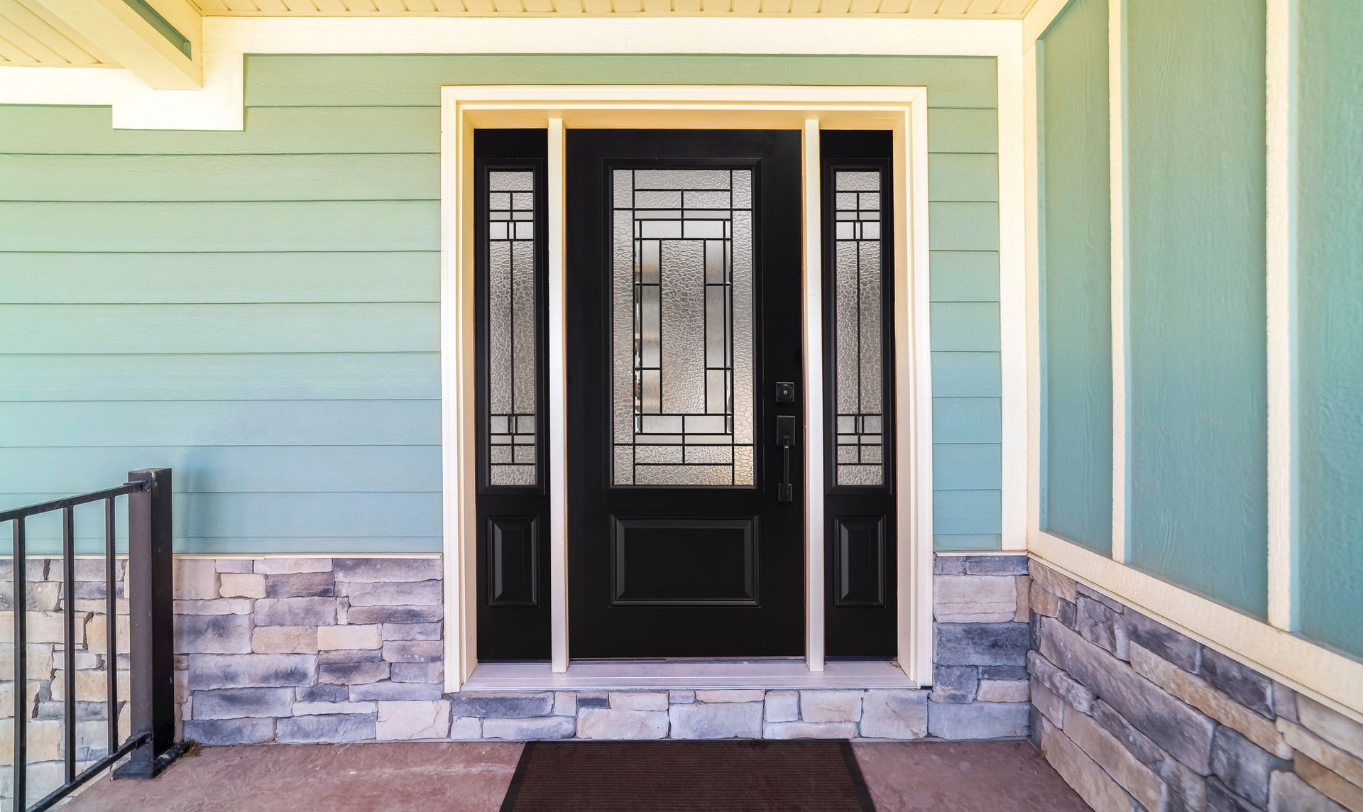 Front porch with a black front door, decorative glass panels, and teal siding with stone trim.