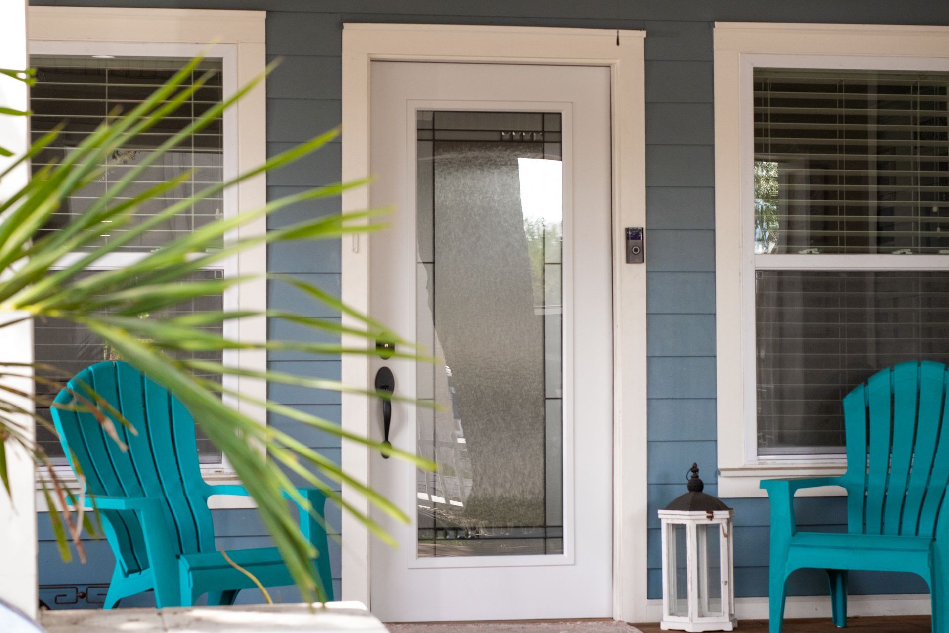 Front porch with white front door, turquoise chairs, and a small lantern beside the entrance.