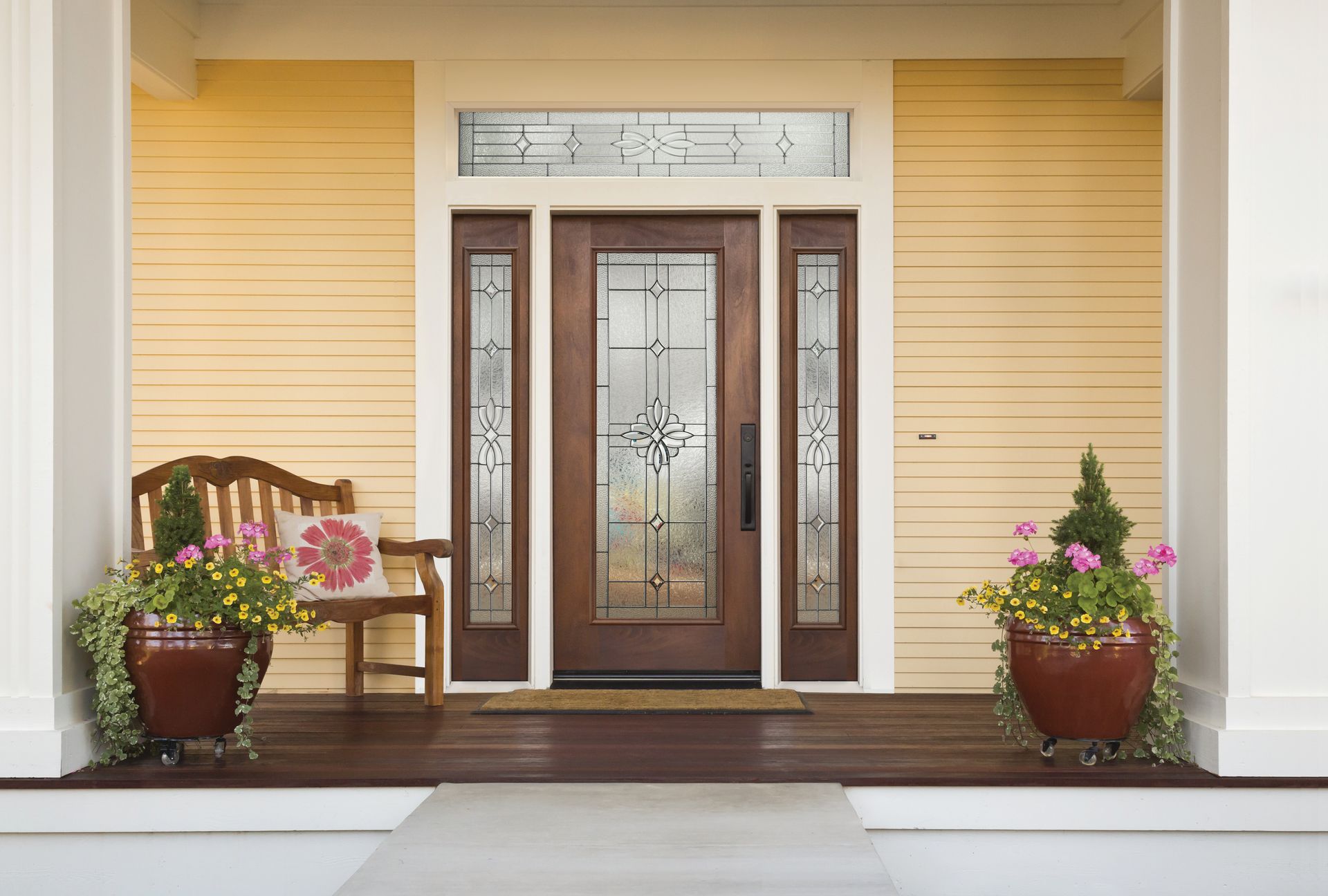 Front porch with double glass doors, yellow siding, a bench, and potted flowers on both sides