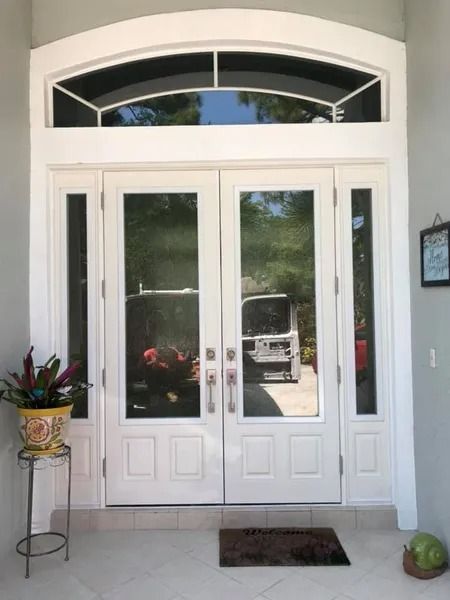 White double entry doors with glass panels and arched transom window; flower pot on a stand beside the door.
