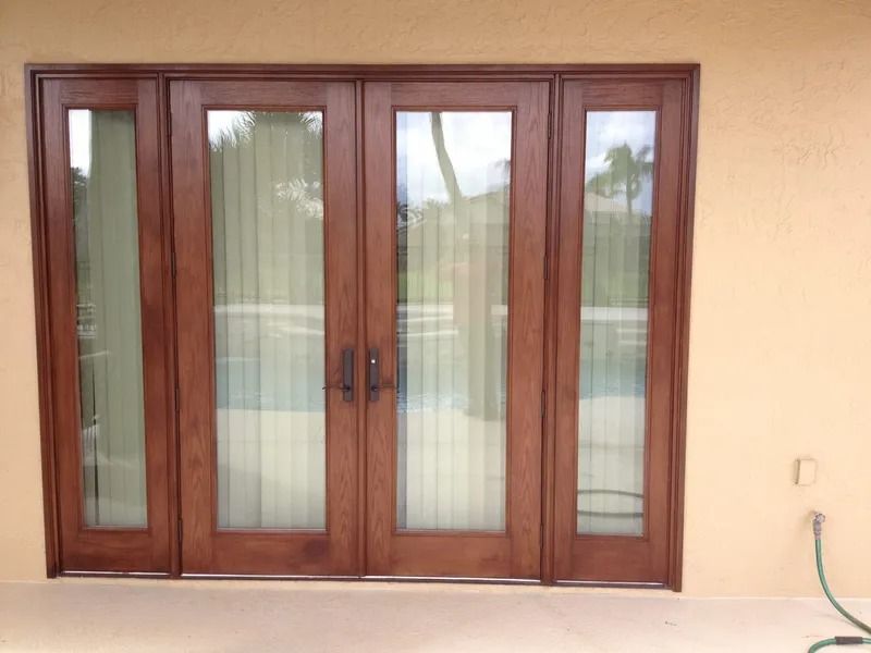 Wooden French doors with glass panes, set in a light beige stucco wall, open onto a patio.