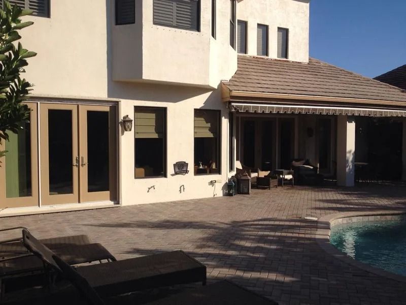 Exterior of a house with a pool, patio, and lounge chairs. Beige walls, brown roof, and blue sky.