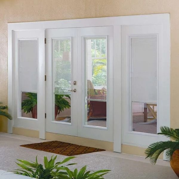 White French doors with sidelights. A doormat and potted plants are in front.
