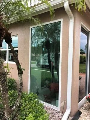 Tan stucco building with a tall window reflecting a tree, and white trim. Gutters are visible.