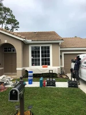 House exterior with a man on the right, tools, and equipment on the lawn. Cloudy sky.