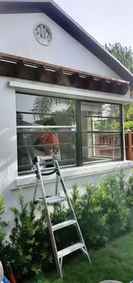 A-frame ladder leaning against a white building with large windows and a decorative overhang.
