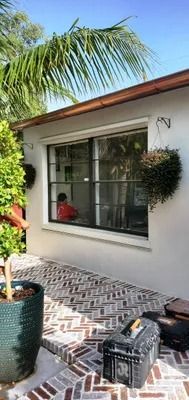 Exterior of a building with a large window. A person sits inside. Brick patio and a potted plant in the foreground.