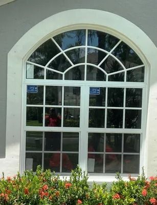 White-framed window with arched top and multiple panes. Reflection of a person in the glass.