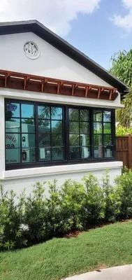 White house with dark windows and wooden accents, lined with green bushes and grass, under a blue sky.