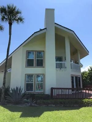 Two-story house with a white exterior, deck, and palm tree against a blue sky.