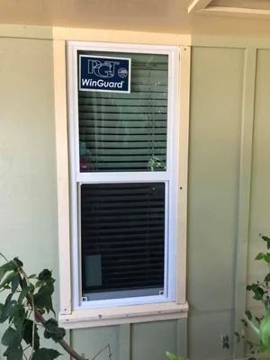 Window with white frame and beige trim, partially obscured by horizontal blinds, set against a pale green wall.