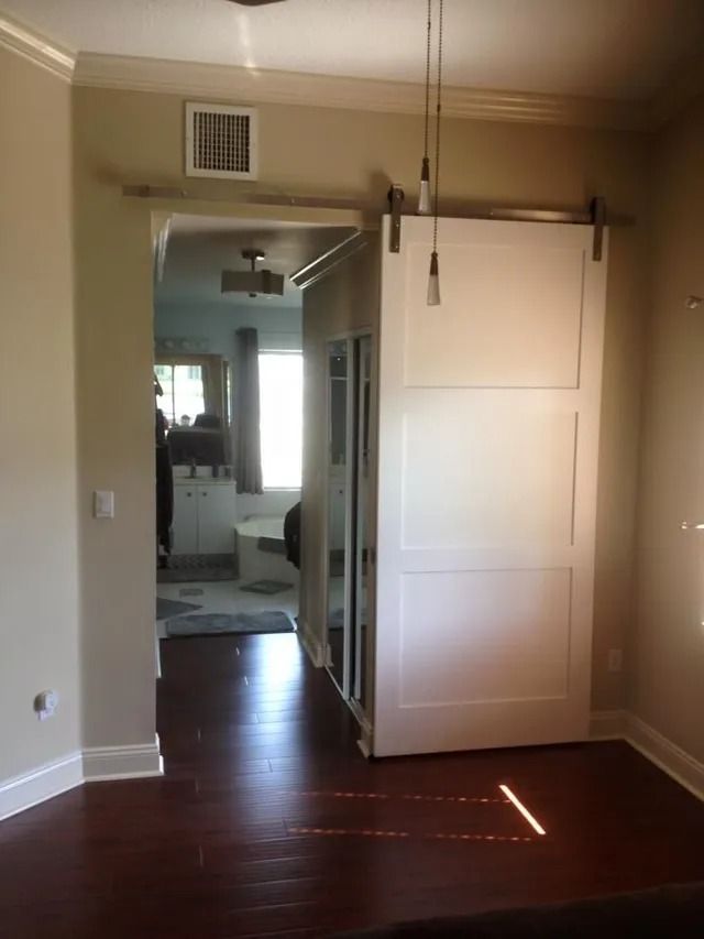White sliding barn door partially open, revealing a living area. Dark wood floor and off-white walls.