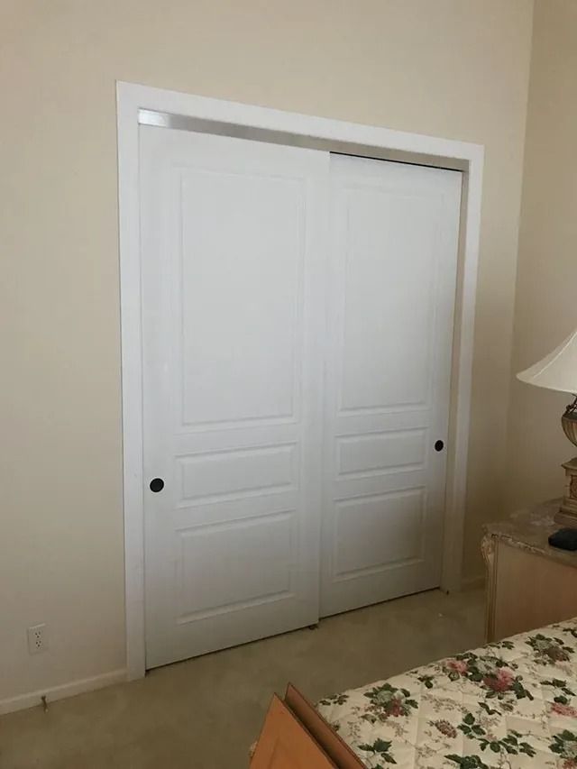 White sliding closet doors with black knobs set in a bedroom with beige walls.