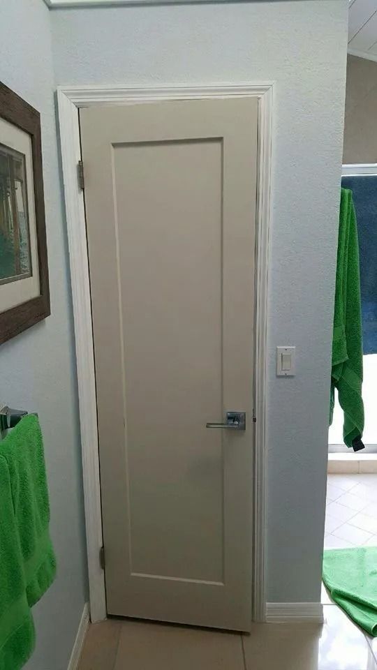 Closed, beige bathroom door with white trim, light blue wall, and green towels.