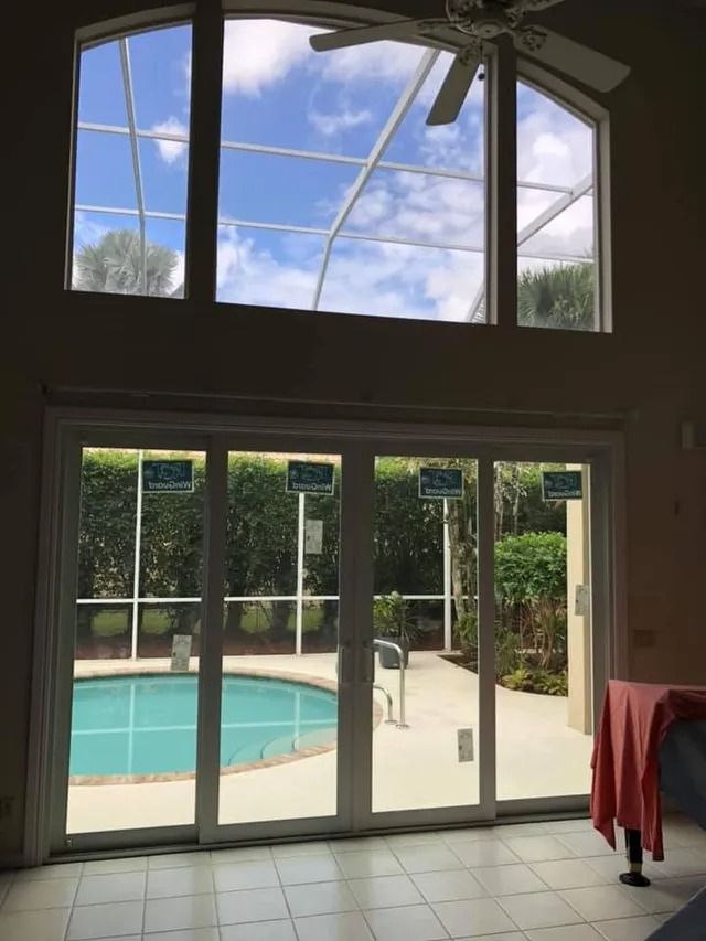 Interior view of a house with large windows and sliding doors, overlooking a pool and lush greenery.