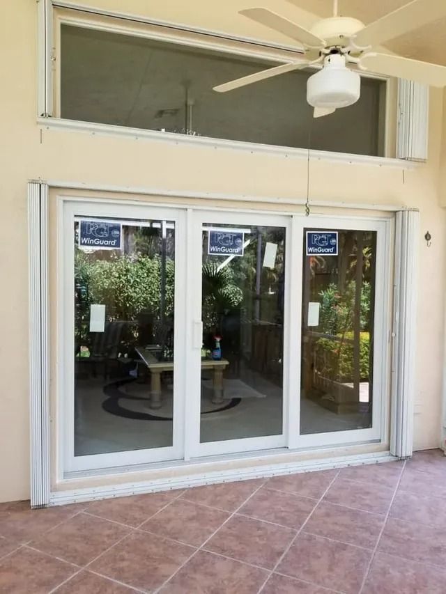 Sliding glass doors with a high transom window, overlooking a patio with furniture and greenery.