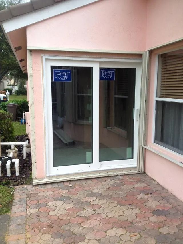 A white-framed sliding glass door on a pink building with a brick patio.