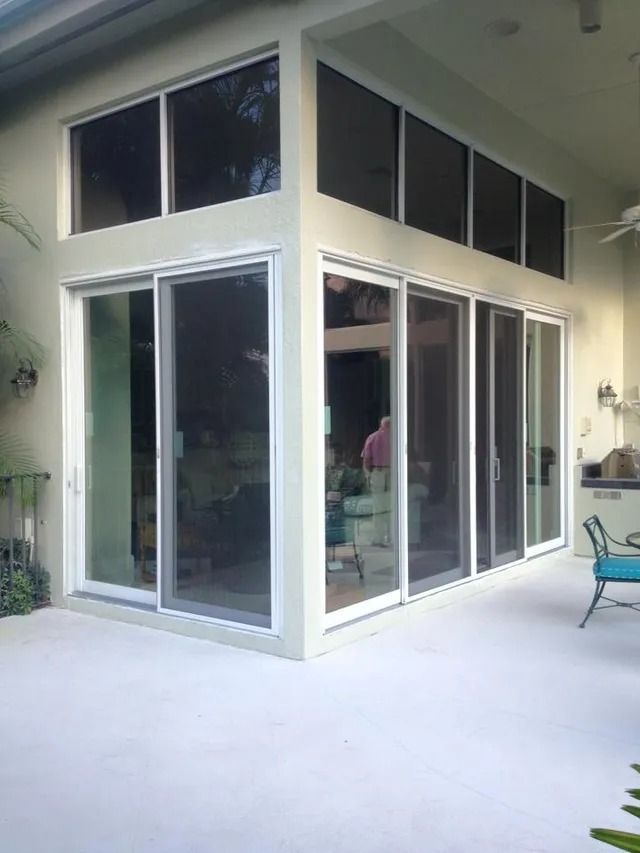 Exterior view of a home with sliding glass doors, upper windows, and a concrete patio.