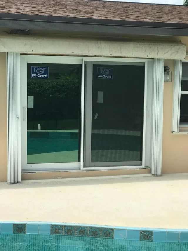Sliding glass door with pool view, white frame, beige exterior, roll-up shutter overhead.