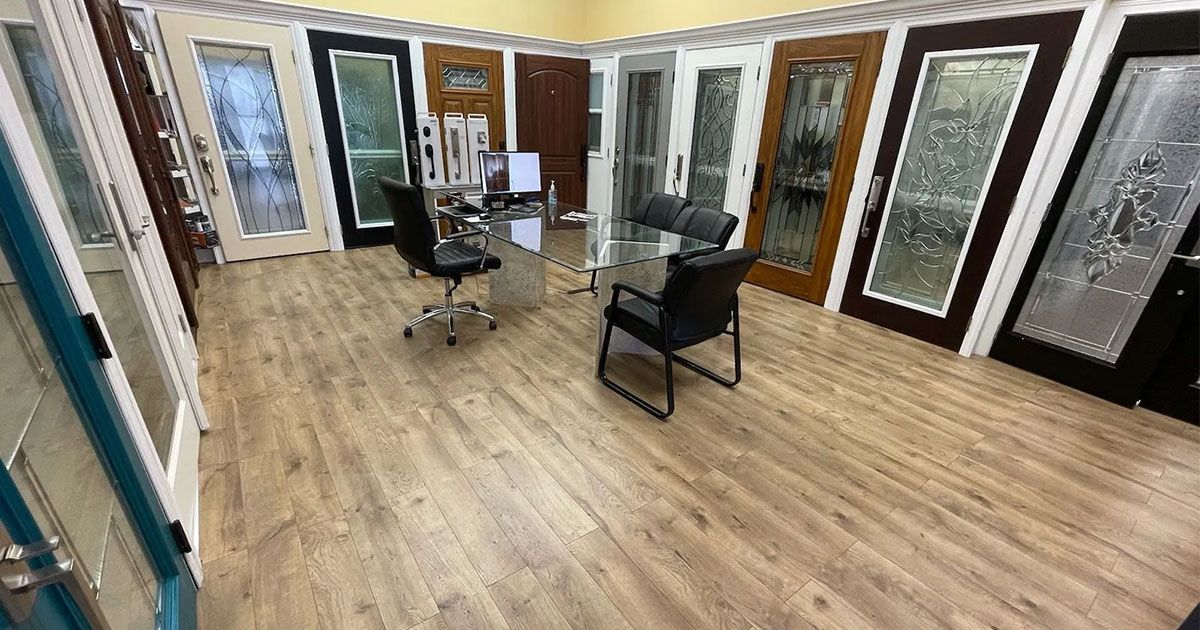 A showroom featuring rows of decorative doors in various styles and finishes, with an office desk and chairs in the center.