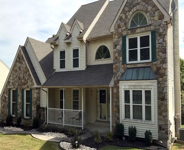 Two-story stone and siding suburban house with front porch, gables, and large windows