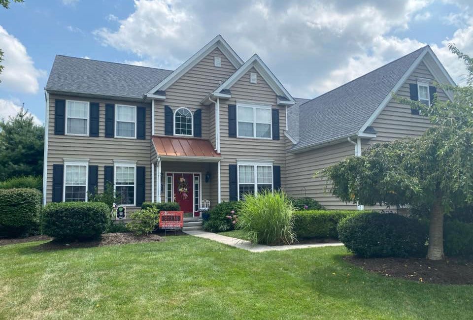 Two-story suburban house with gray siding, red front door, and manicured lawn under a partly cloudy sky