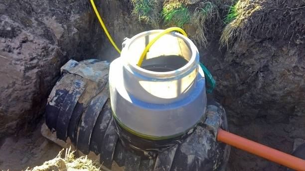 A septic tank being installed in a ditch with a yellow pipe and open gray lid.